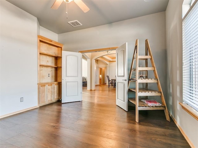 empty room with arched walkways, ceiling fan, dark wood-type flooring, and visible vents