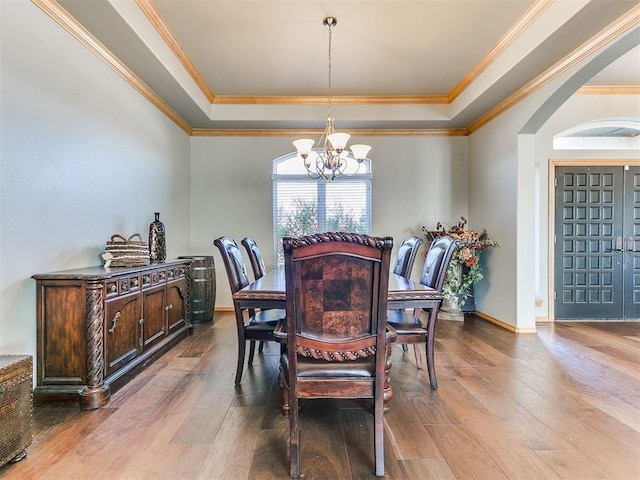 dining room featuring a chandelier, wood finished floors, arched walkways, and a raised ceiling