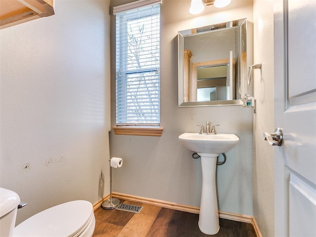 half bath featuring toilet, plenty of natural light, and wood finished floors