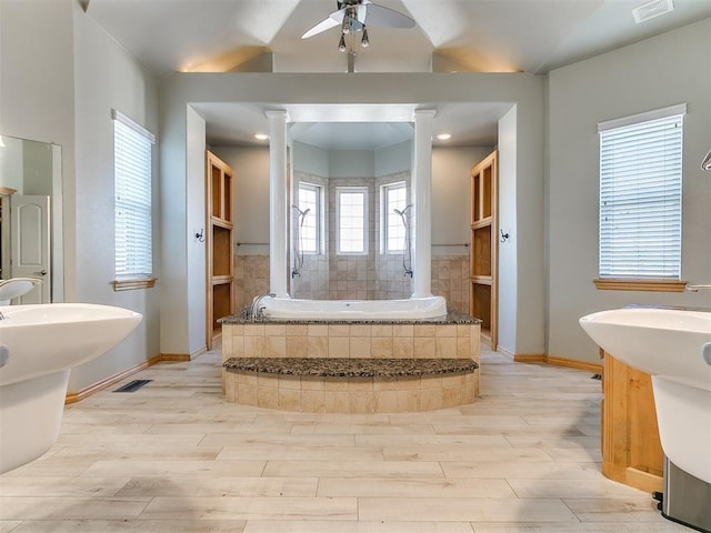 bathroom featuring wood finished floors, visible vents, vaulted ceiling, a bath, and decorative columns