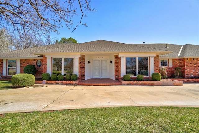 ranch-style house featuring french doors, brick siding, and roof with shingles