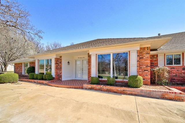 single story home with french doors, brick siding, and roof with shingles