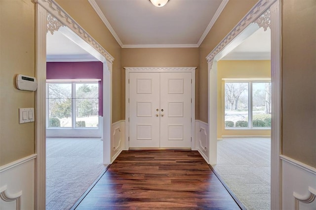 interior space with a wainscoted wall, dark wood-type flooring, ornamental molding, and dark carpet