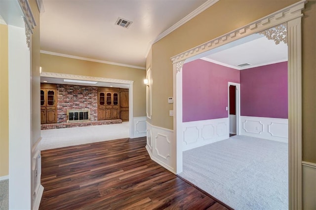 hallway featuring visible vents, wood finished floors, crown molding, and a wainscoted wall