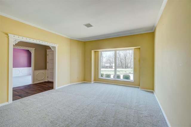 carpeted spare room featuring visible vents, wainscoting, baseboards, and ornamental molding