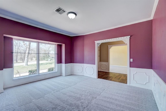 carpeted empty room featuring visible vents, wainscoting, and crown molding