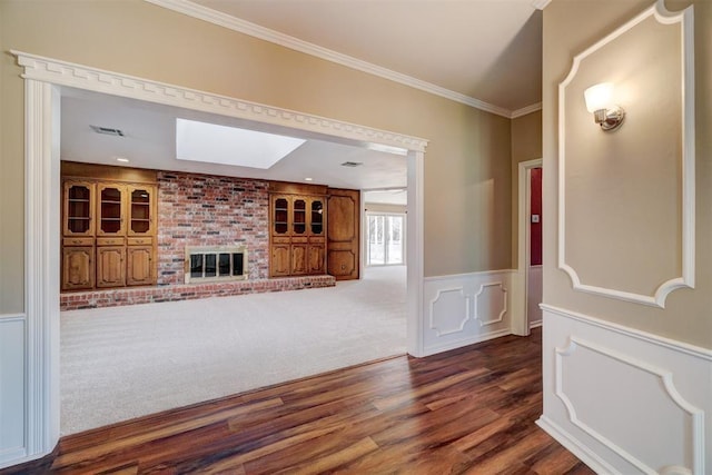 unfurnished living room with visible vents, dark wood-type flooring, ornamental molding, a skylight, and wainscoting