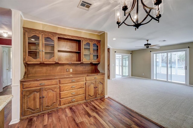 kitchen featuring visible vents, brown cabinets, ceiling fan with notable chandelier, crown molding, and glass insert cabinets