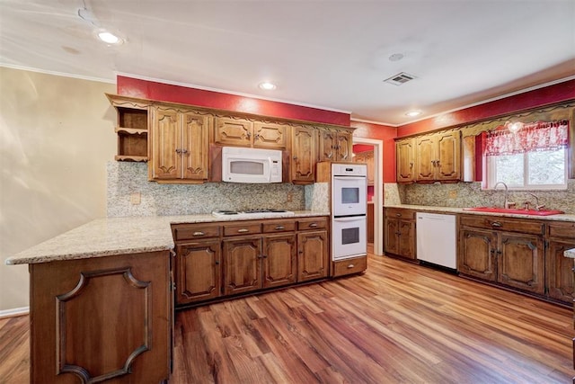 kitchen with white appliances, wood finished floors, visible vents, a peninsula, and a sink