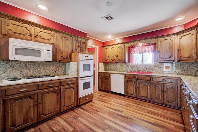 kitchen featuring visible vents, a sink, white appliances, light wood finished floors, and decorative backsplash