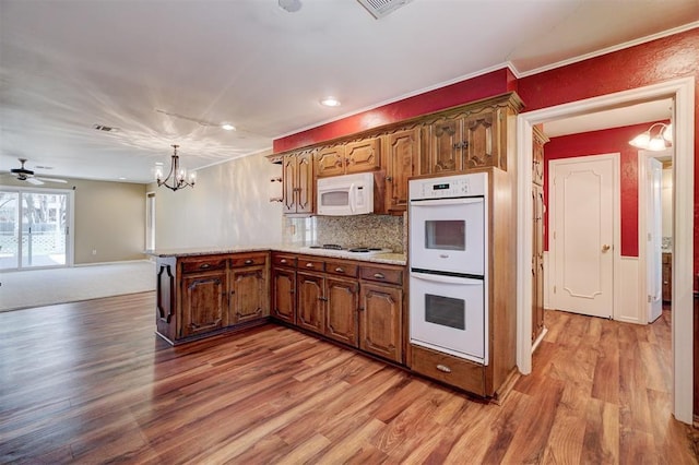 kitchen featuring decorative backsplash, white appliances, light wood-style floors, and a peninsula