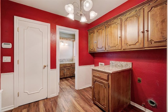 washroom with wood finished floors, an inviting chandelier, cabinet space, washer hookup, and wainscoting