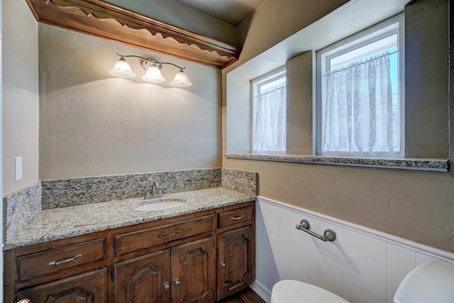 bathroom featuring a wainscoted wall, toilet, and vanity