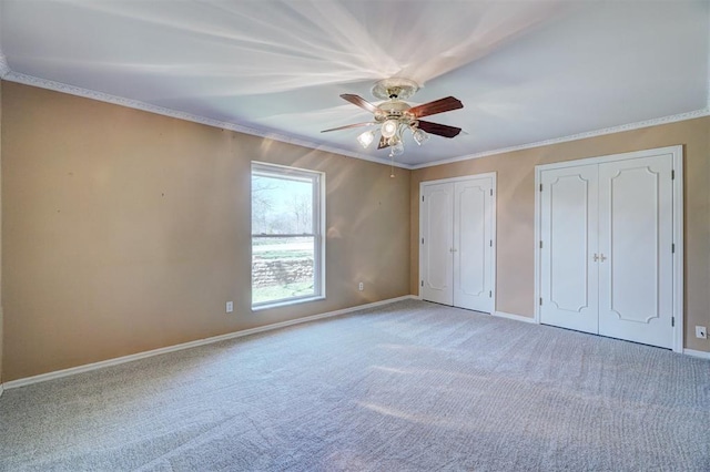 unfurnished bedroom featuring crown molding, ceiling fan, baseboards, multiple closets, and light carpet