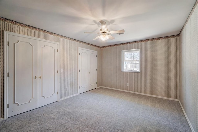 unfurnished bedroom featuring baseboards, carpet flooring, wallpapered walls, and multiple closets