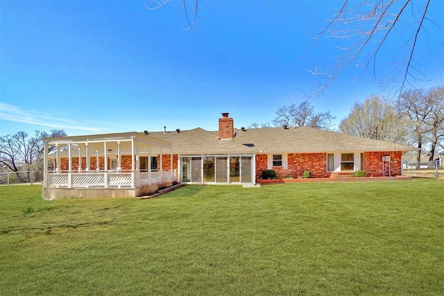 back of house with brick siding, fence, a chimney, a yard, and a sunroom