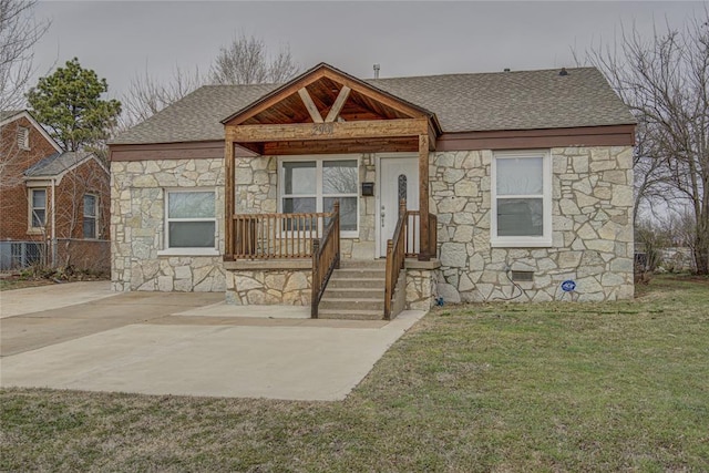 bungalow-style home with a porch, stone siding, roof with shingles, and a front lawn