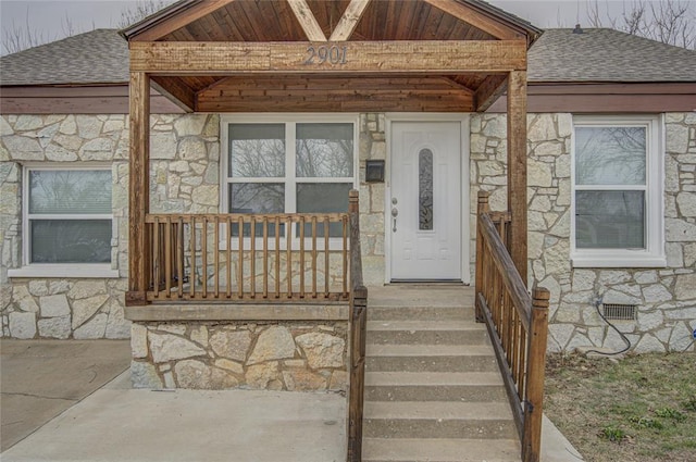 view of exterior entry with crawl space, stone siding, a shingled roof, and covered porch