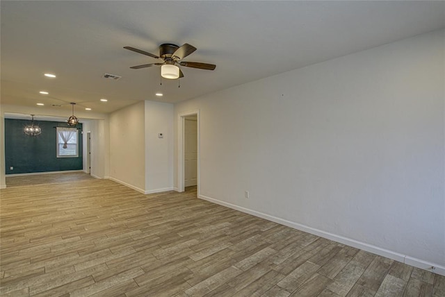 unfurnished room featuring ceiling fan with notable chandelier, wood finished floors, visible vents, and baseboards