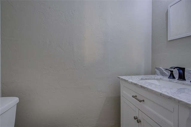 bathroom featuring toilet, a textured wall, and vanity