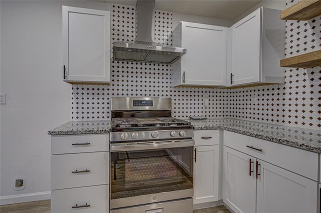 kitchen featuring white cabinets, wall chimney exhaust hood, stainless steel range with gas stovetop, light stone countertops, and backsplash