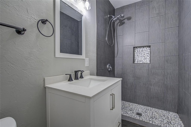 full bathroom featuring a textured wall, tiled shower, and vanity