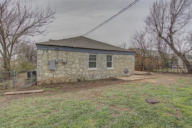 view of side of property with stone siding, fence, a lawn, and roof with shingles