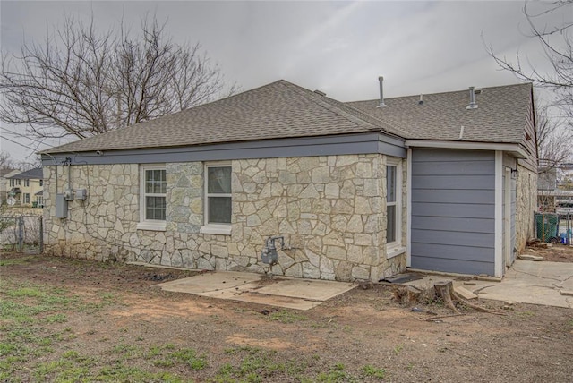 rear view of house featuring stone siding, a shingled roof, and fence