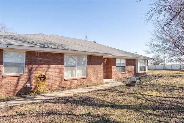 rear view of house with a shingled roof, a yard, brick siding, and fence