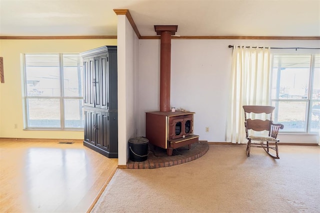 sitting room featuring carpet floors, visible vents, baseboards, a wood stove, and crown molding