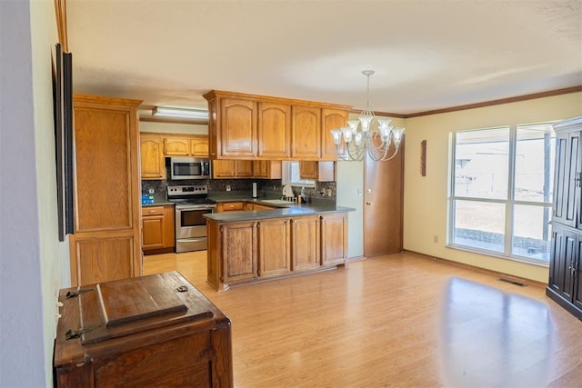 kitchen with tasteful backsplash, brown cabinetry, appliances with stainless steel finishes, a peninsula, and an inviting chandelier