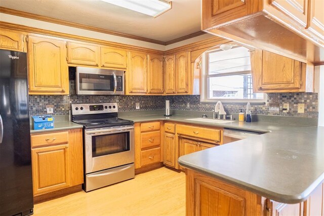 kitchen featuring light wood finished floors, ornamental molding, a peninsula, stainless steel appliances, and a sink