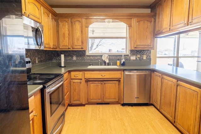 kitchen with appliances with stainless steel finishes, brown cabinets, a sink, light wood-style floors, and backsplash