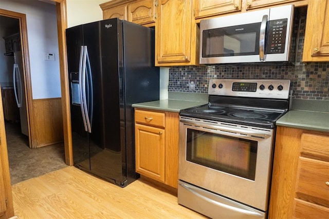 kitchen with a wainscoted wall, appliances with stainless steel finishes, brown cabinetry, and light wood-style flooring