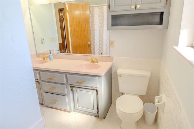 full bath with double vanity, wainscoting, toilet, a sink, and tile walls