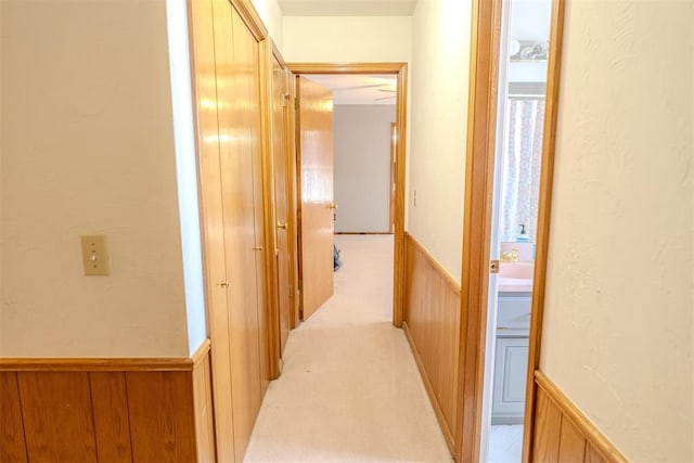 corridor with a textured wall, light colored carpet, wood walls, and wainscoting