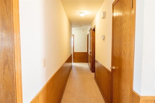 corridor featuring a wainscoted wall, light carpet, and wooden walls