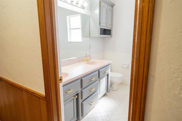 full bathroom with a wainscoted wall, double vanity, toilet, a sink, and tile patterned floors