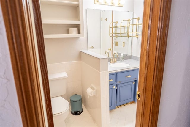 bathroom featuring wainscoting, tile walls, toilet, and vanity