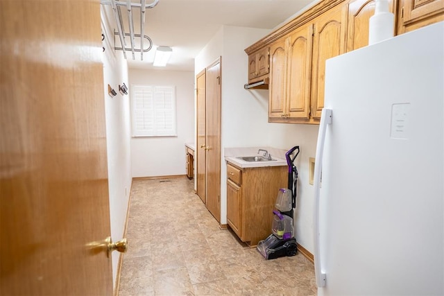 kitchen with freestanding refrigerator, light countertops, a sink, and baseboards