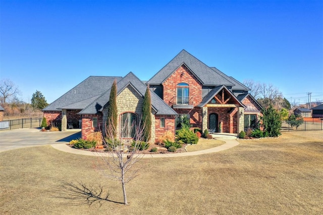 craftsman-style home with brick siding, a shingled roof, fence, stone siding, and driveway