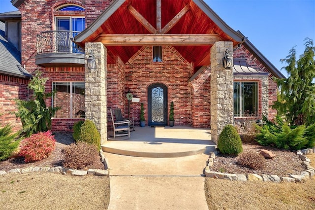 entrance to property featuring covered porch, brick siding, and a balcony