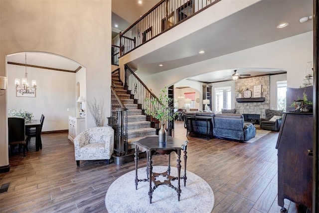 entrance foyer featuring arched walkways, a fireplace, ornamental molding, stairway, and dark wood finished floors