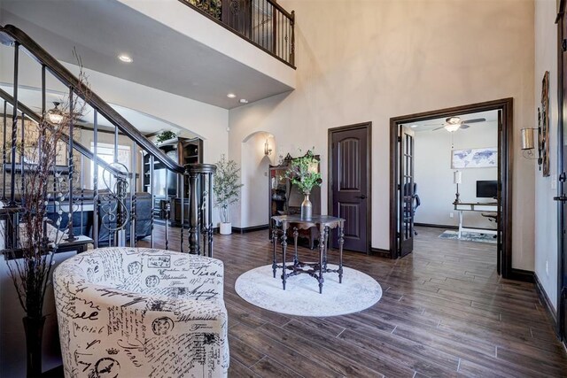 entryway with arched walkways, stairway, dark wood-type flooring, ceiling fan, and baseboards