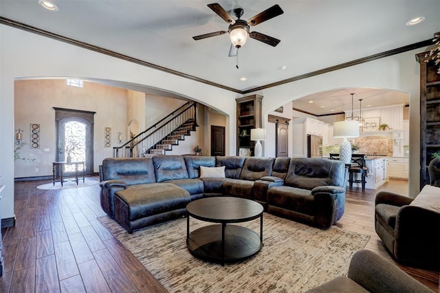 living room featuring arched walkways, recessed lighting, wood finished floors, baseboards, and stairway