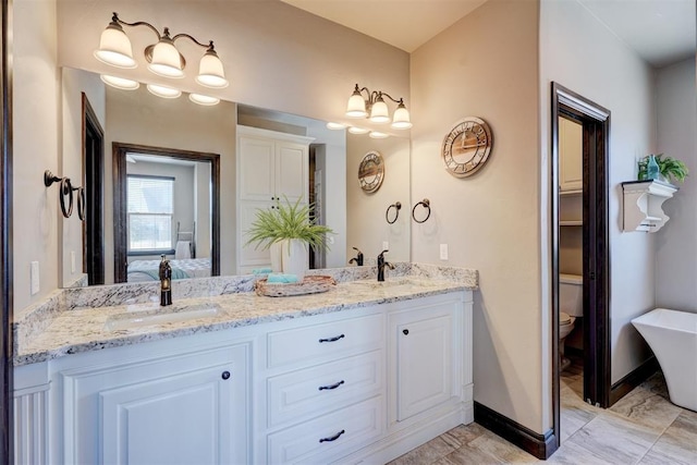 full bath featuring toilet, a sink, baseboards, double vanity, and ensuite bath