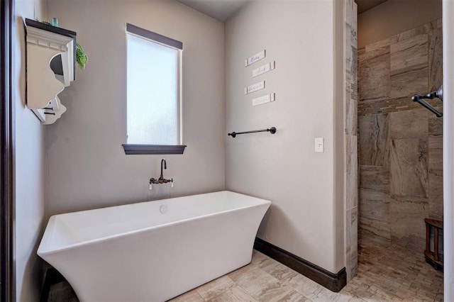 bathroom featuring a freestanding bath, a tile shower, and baseboards