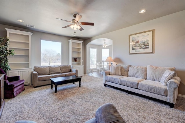 living area with visible vents, arched walkways, a ceiling fan, carpet flooring, and built in shelves