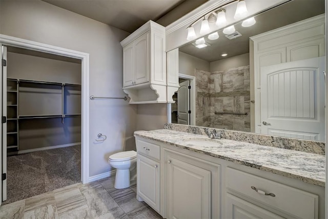 bathroom featuring baseboards, toilet, a spacious closet, a tile shower, and vanity