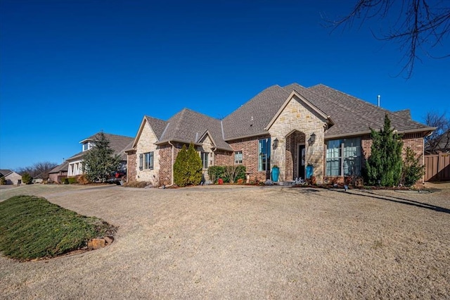 french country inspired facade with stone siding, fence, and brick siding